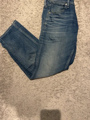 Blå Jack & Jones jeans 28/30 - Klassiska blå jeans med vanlig passform och fem fickor. Jeansen har en snygg tvättad look och är tillverkade i slitstarkt bomullsdenim. Perfekta för dig som gillar tidlös stil och vill ha ett par jeans som funkar till allt. Storlek 28/30