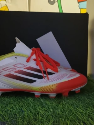 Adidas vita och röda fotbollsskor - Snygga fotbollsskor från Adidas i vitt med röda och svarta detaljer samt röda snören. Skorna har en låg profil och är tillverkade i syntetmaterial med mönstrad ovandel och fasta dobbar för bra grepp på planenköptes för 750.