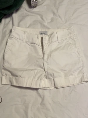 Vita shorts från GANT - Klassiska vita shorts från GANT med normal passform. De har hällor för bälte, fickor fram och bak samt stängs med dragkedja och knapp. Perfekta för sommaren och lätta att matcha med allt. Snygg och stilren look!