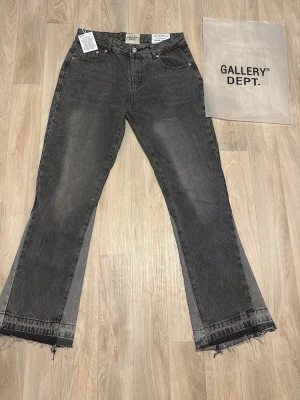 Grå bootcut jeans från Gallery Dept. - Säljer ett par gråa flared  jeans från Gallery Dept. Jeansen har råa, fransiga benslut och en bredare passform nertill. Klassisk femficksmodell med knappar och dragkedja. Materialet är jeans i bomull och färgen är mörkgrå med slitningar.