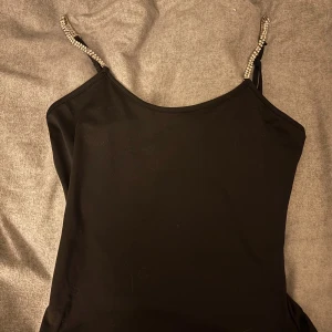 Svart linnetopp med glittriga axelband - Snygg svart linnetopp med glittriga axelband som ger en extra touch. Perfekt för en kväll ute. Är innan en body men klippt längst ner. Inte jätte bra klippt men går lätt att bara klippa själv annars viks den upp av sig själv när man sätter på sig den🩷