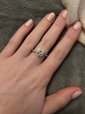 Silverfärgad ring med hjärta och stenar - Säljer en snygg silverfärgad ring med ett hjärtformat motiv i mitten, dekorerad med gnistrande små stenar runt om. Ringen har en tunn banddesign och passar perfekt för dig som gillar romantiska detaljer och bling.Vid köp av fler ringar kan jag slå ihop annonserna så frakten blir billigare.