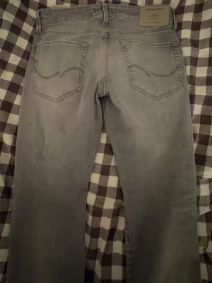 Gråa jeans från Jack & Jones - Snygga gråa jeans från Jack & Jones med klassisk femficksdesign och raka ben. Jeansen har en ljus tvätt och subtila slitningar framtill för en avslappnad look. Perfekta till vardags och lätta att matcha med olika stilar. Modell-slim glenn STorlek 28/30. Nypris 799