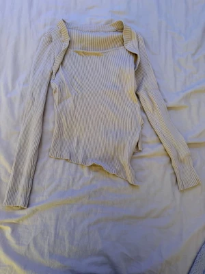 Beige ribbad topp från SHEIN - Trendig beige långärmad topp från SHEIN med ribbad struktur och asymmetrisk nederkant. Toppen har en bred, fyrkantig ringning och är gjord i ett mjukt stretchigt material som sitter snyggt på kroppen. Perfekt för dig som gillar unika detaljer och stilren design.