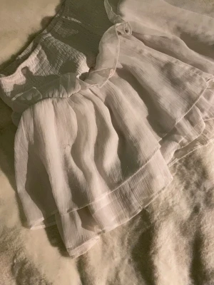 Vit volangkjol med resårmidja - Supersöt vit kjol med dubbla volanger och resår i midjan. Kjolen är gjord i ett lätt, skirt tyg som ger en luftig känsla och har en fin struktur. Perfekt för dig som gillar romantiska detaljer och vill ha en flowy look.