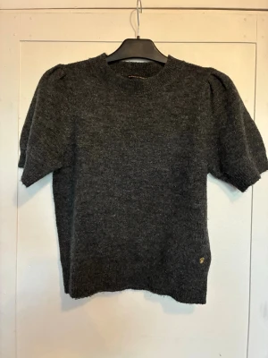 Mörkgrå stickad topp med puffärm - Mysig mörkgrå stickad topp med korta ärmar och rund hals. Jättesnygg men passar tyvärr inte mig. Knappt använd- i nyskick. Från Pernilla Wahlgrens kollektion.