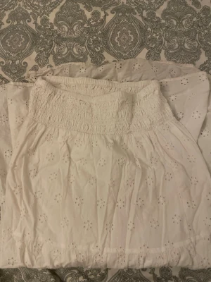 Vit kortkjol från Gina Tricot - Söt vit kortkjol från Gina Tricot med broderade blommor och bred smock i midjan. Kjolen ger en fin sommar vibe