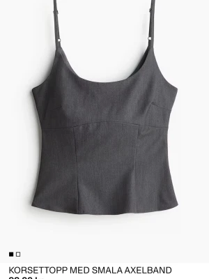 Mörkgrå korsettopp med smala axelband - Stilren mörkgrå korsettopp med smala justerbara axelband och i figurnära modell. Toppen har iögonfallande sömmar på framsidan för en snygg siluett. Perfekt att styla med både jeans och kjol.