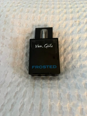 Van Gils Frosted parfym - Van Gils Frosted parfym i en stilren, svart glasflaska med blå och vit text. Flaskan har en rektangulär form och ett metallfärgat spraymunstycke. Perfekt för dig som gillar moderna och fräscha dofter.