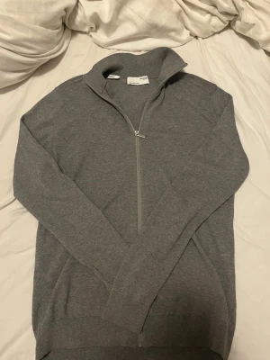  Selected Homme grå kofta  - Säljer en stilren grå kofta från Selected Homme. Tröjan har lång ärm, hög krage och hel dragkedja framtill. Tillverkad i mjukt material som känns skönt mot huden. Perfekt för lager på lager under kyligare dagar.