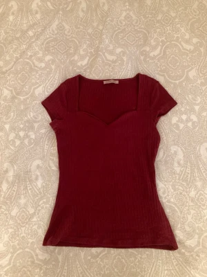 Vinröd ribbad topp med sweetheart-ringning - Snygg vinröd topp med ribbad struktur och korta ärmar. Skriv om du har några frågor!
