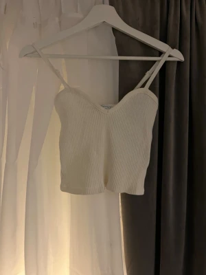 Vit ribbad croppad linnetopp - Säljer en vit croppad linnetopp från Zara med smala justerbara axelband och v-ringad urringning. Toppen är ribbad och har en mjuk, stretchig känsla som gör den superbekväm och enkel att styla till olika looks.