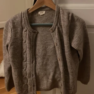 Beige stickad kofta från Noa Noa - Mysig beige stickad kofta från Noa Noa med fina flätade detaljer längs knappraden. Koftan har rund halsringning, långa ärmar och stängs med träknappar. Perfekt att slänga över en topp för en chill look.