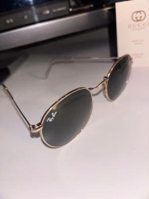 Rayban solglasögon  - Ray-Ban solglasögon – klassisk modell  Snygga Ray-Ban solglasögon i guldfärgad metall med mörka glas. Klassisk och tidlös modell som passar både dam och herr. Glasen är i bra skick och bågarna är hela. Bekväma att bära och perfekta till både vardag och sommar.  Säljes i befintligt skick. Hör av dig vid frågor eller intresse.