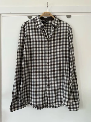 Filippa K skjorta - Klassisk rutig skjorta från Filippa K i storlek M i brunt, vitt och grått. Bekväm krage och dubbla knappar vid ärmsluten för bästa passform. 100% bomull, så bra material som andas. Fint skick!! Nypris 1800:-  Hämtas i Stockholm eller skickas mot porto.