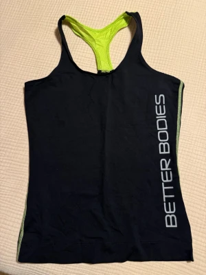 Svart träningslinne från Better Bodies - Svart träningslinne med limefärgade detaljer från Better Bodies med brottarrygg i storlek S. Använt fåtal gånger, fint skick.