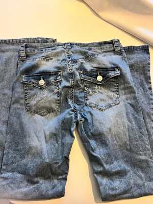 Blå jeans med fickdetaljer från Molly - Snygga ljusblå jeans från nelly med raka ben och dekorativa bakfickor med knappar och vit söm. Klassisk femficksmodell och knappgylf. Perfekta till vardagslooken och lätta att matcha med olika stilar.