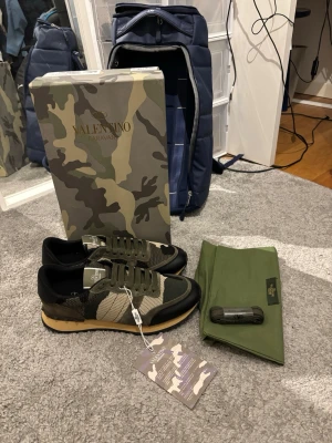 Valentino Garavani camo sneakers - Snygga sneakers från Valentino Garavani i en mix av grönt, beige och svart med coolt camouflagemönster. Skorna har snörning, platt sula och detaljer i mesh och skinn. Perfekta för dig som vill sticka ut med exklusiva och trendiga sneakers.