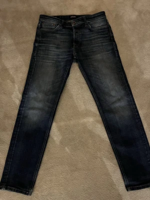 Jack & Jones Tapered Mike jeans blå - Säljer ett par mörkblå jeans från Jack & Jones, modell Tapered Mike. Jeansen har lite lite slitningar på baksidan som man kan se på bilden men annars är de i bra skick