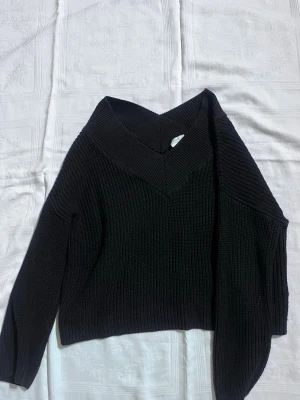 Svart ribbad stickad tröja NA-KD - Säljer en svart ribbad stickad tröja från NA-KD x Pamela. Tröjan har en bred v-ringad krage och lång ärm. Perfekt till höst och vinter när du vill vara både varm och snygg. Passformen är normal och materialet känns mjukt och rejält.