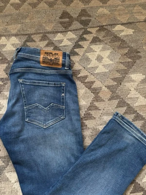 Replay Anbass blå jeans herr - Säljer ett par Replay Anbass jeans i klassisk blå tvätt med snygga slitningar. Modellen har fem fickor, normal passform och raka ben. En liten vit fläck på framsidan finns, men som man inte lägger märke till. 100 cm i längd