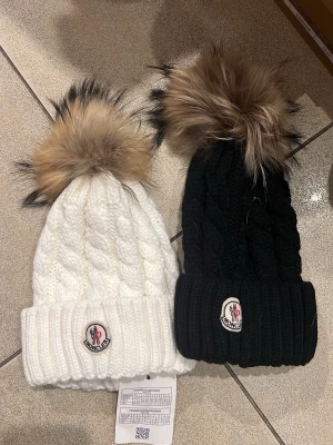 Svart ribbstickad mössa med pälsboll - Snygg svart ribbstickad mössa med stor fluffig pälsboll på toppen. Klassisk uppvikt kant och trendig design som passar perfekt till kalla dagar. Materialet känns mjukt och värmande.