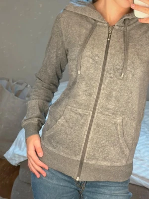 Grå zip hoodie med huva! - Mysig grå hoodie med dragkedja framtill och två stora fickor. Tröjan har huva med dragsko och ribbade muddar vid ärmar och nederkant. Perfekt för en avslappnad look och enkel att matcha med jeans eller träningskläder.