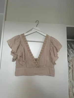 Beige croppad blus med volangärm - Supersöt beige croppad blus med djup v-ringning och spetsdetaljer längs urringningen. Blusen har volangärmar ❣️⭐️