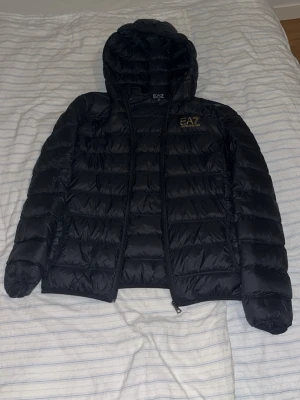 Svart dunjacka med huva från EA7 - Säljer min EA7 pufferjacka. Jackan är helt äkta och i bra skick. Den håller värmen bra och funkar perfekt till vardags.  Storlek: S / 175 cm Skick: Bra, enda anmärkningen är lätt slitage som syns vid närmare titt. Inga hål, revor eller större skador.  Pris kan diskuteras vid snabb dm. Skriv om du vill ha fler bilder eller info.