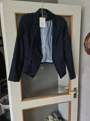 Mörkblå kavaj med fickor - Stilren mörkblå kavaj med klassisk krage och två framfickor. Insidan har ett ljusblått, randigt foder som ger en snygg kontrast. Perfekt för dig som vill ha en tidlös och mångsidig look.