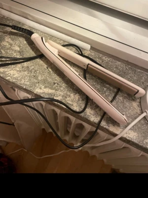 Ljusrosa plattång med sladd - Säljer en ljusrosa plattång med keramiska plattor och lång svart sladd. Perfekt för att styla håret rakt eller skapa mjuka vågor. Enkel att använda och smidig att ta med sig. Passar dig som vill fixa frisyren snabbt och enkelt.