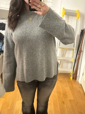 Grå oversized stickad tröja - Mysig grå stickad tröja med oversized passform och breda ribbade muddar vid ärmslut och nederkant. Tröjan har en hög, ribbad rund halsringning och är tillverkad i ett mjukt material som känns skönt mot huden. Perfekt för lager på lager och chill dagar. Lite nopprig men går nog att få bort.