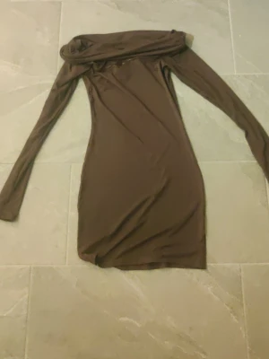 Brun långärmad klänning från Divided - Snygg brun långärmad klänning från Divided  (HM) med offshoulder-krage. Klänningen är figurnära och har en kort längd, perfekt för dig som gillar en enkel men trendig stil. Tillverkad i mjukt material som känns skönt mot huden. Inga synliga fläckar och aldrig använd. Klänningen är i storlek S. 