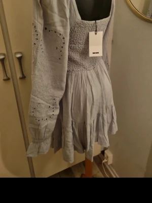 Ljusblå kortklänning från Bik Bok - Supersöt ljusblå kortklänning från Bik Bok med smockad överdel, volangkant nertill och broderade detaljer på ärmarna. Klänningen har långa ärmar och en luftig, flowy passform som känns perfekt för varmare dagar.