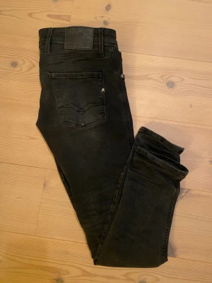 Svarta Replay Anbass jeans - Säljer ett par svarta Replay Anbass jeans med klassisk femficksdesign och diskret Replay-logga på bakfickan. Jeansen har smal passform och är tillverkade i stretchigt bomullsmaterial för extra komfort. Snyggt slitna detaljer och mörk tvätt ger en cool look. Storlek 30/32. Kontakta mig om frågor!😊