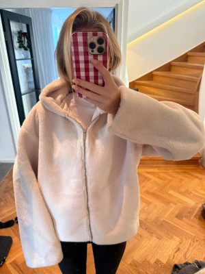 Ljusbeige teddyjacka med huva - Supermjuk och fluffig teddyjacka i ljusbeige med dragkedja framtill och stor huva. Jackan har en loose passform och långa ärmar, perfekt för kalla dagar. Enkel och clean look som är lätt att styla till allt.