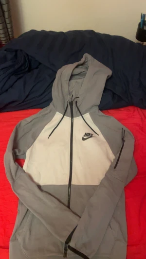 Nike hoodie i grått och vitt - Snygg hoodie från Nike i grått och vitt med svart logga på bröstet. Tröjan har hel dragkedja, huva med snörning och praktiska fickor. Perfekt för chill eller träning, och passar till allt. Klassisk streetstil med bekväm passform.