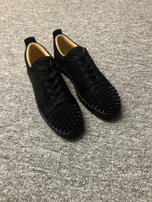 Christian Louboutin svarta sneakers med nitar - Svarta sneakers från Christian Louboutin i mocka med coola svarta nitar på tån och klassisk röd sula. Helt nya fick som present av farsan gick ej att lämna tillbaka