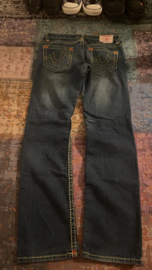 True Religion jeans med kontrastsömmar - Säljer ett par blå True Religion jeans med tydliga gröna kontrastsömmar och klassiska bakfickor med broderad logga. storlek 29. skriv för mått.