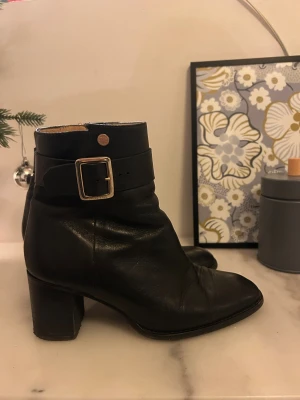 Svarta boots med klack från Novita - Snygga svarta boots från Novita i skinn med rund tå och stabil klack. Dekorativt spänne i guld och dragkedja på sidan för enkel påtagning. Köpt för 700. Meddela för mer frågor, bilder eller diskutera pris 💛💛