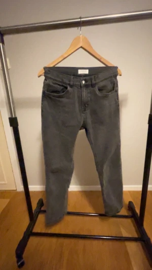 Grå jeansbyxor från Lindex, strl 158 - Snygga grå jeansbyxor från Lindex i klassisk femficksmodell. Byxorna har rak passform och normal midja, perfekta för en avslappnad stil. Tillverkade i mjukt bomullsmaterial med dragkedja och knapp framtill.