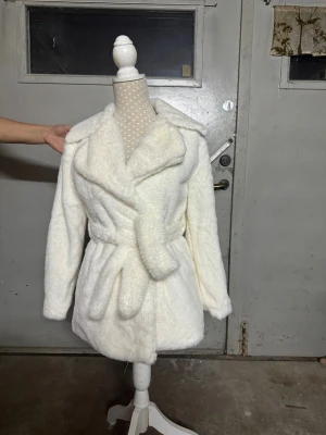Vit pälsjacka med bälte - Säljer en fluffig vit teddyjacka med bred krage och bälte i midjan. Jackan har lång ärm och är tillverkad i mjukt, pälsliknande material som ger en riktigt cozy vibe. Perfekt för dig som vill ha en varm och stylish look under kyliga dagar. Använd 2-3 gånger i helt nytt skick ! 