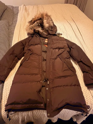 Brun lång dunjacka Parajumpers M - Säljer en brun lång dunjacka från parajumper , modell Long Bear Woman. Jackan har en stor huva med päls, flera fickor med dragkedja och snygga detaljer. Slim fit och perfekt för kalla vinterdagar.