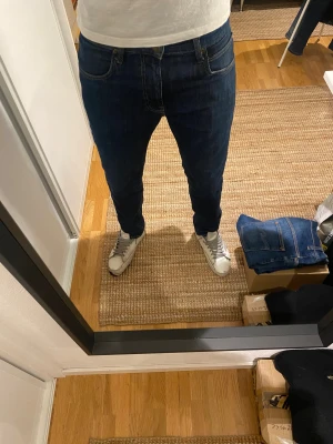 Mörkblå slim jeans från Lee - Säljer ett par mörkblå slim jeans från Lee med klassisk femficksdesign och brunt Lee-märke bak i midjan. Jeansen har smal passform, raka ben och är tillverkade i mjukt denimtyg med snygga kontrastsömmar. Jeansen är helt nyinköpta och endast använda en gång! Tveka inte att höra av er om ni har frågor eller prisförslag. Nypris på dessa är 1199, mitt pris: 399