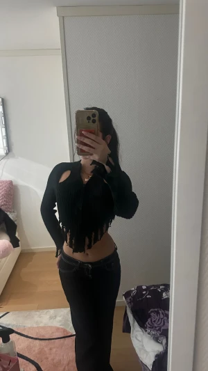 Svart croppad stickad tröja med slitningar - Svart croppad stickad tröja med långa ärmar och coola slitningar längs nederkant och ärmslut. Tröjan har ribbad struktur och unika cut-outs vid axlarna för en edgy vibe. Perfekt för dig som vill sticka ut med din stil.