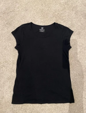 Svart basic t-shirt från H&M - En enkel svart t-shirt från H&M i ekologisk bomull. Modellen är klassisk med rund hals och korta ärmar, perfekt för en clean och stilren look. Passar dig som gillar basic och vill ha en mjuk och skön t-shirt i garderoben.