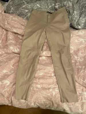 Beige skinnbyxor från Zara - Snygga beige skinnbyxor från Zara i storlek L. Byxorna har en rak och slim passform med hög midja och dragkedjor vid bensluten. Materialet är mjukt syntetiskt skinn med mockaliknande insida för extra komfort. Perfekt för dig som gillar stilrena och trendiga plagg. OBS! Endast testade! Säljer pgaatt det går ej att lämna tillbaka då jag har slängt prislappen.