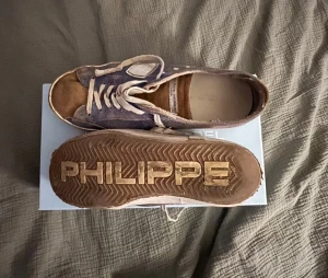 Philippe Model blå sneakers strl 41 - Pris kan diskuteras! Säljer ett par snygga Philippe Model sneakers i blått och beige med vita snören. Skorna har rund tå, platt sula och coolt PHILIPPE-tryck under sulan. Materialet är en mix av mocka och skinn, vilket ger en lyxig känsla. Perfekt för dig som gillar streetstyle och fransk design.