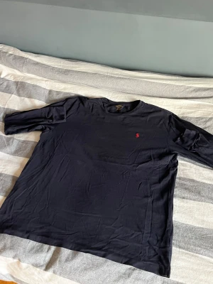 Marinblå långärmad t-shirt från Polo Ralph Lauren - Svart långärmad t-shirt från Polo Ralph Lauren med klassisk röd broderad logga på bröstet. Tillverkad i 100% bomull för en skön och mjuk känsla. Enkel och stilren design som funkar till det mesta.