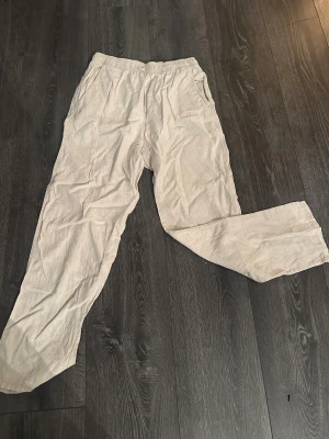 Beiga linnebyxor från H&M - Säljer ett par beiga linnebyxor från H&M med resår i midjan och raka ben. Byxorna har sidfickor och är tillverkade i 100% linne, vilket gör dem luftiga och perfekta för varmare dagar. Enkel och avslappnad stil som passar till det mesta.